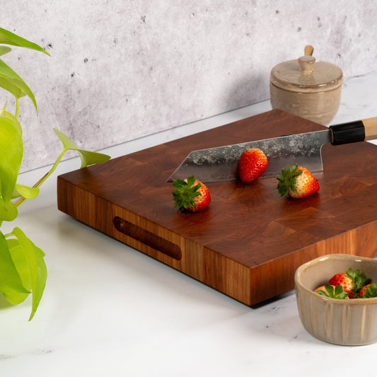 Cherry cutting board on a marble kitchen counter top, square cutting board cherry wood, fresh strawberries, neon pothos