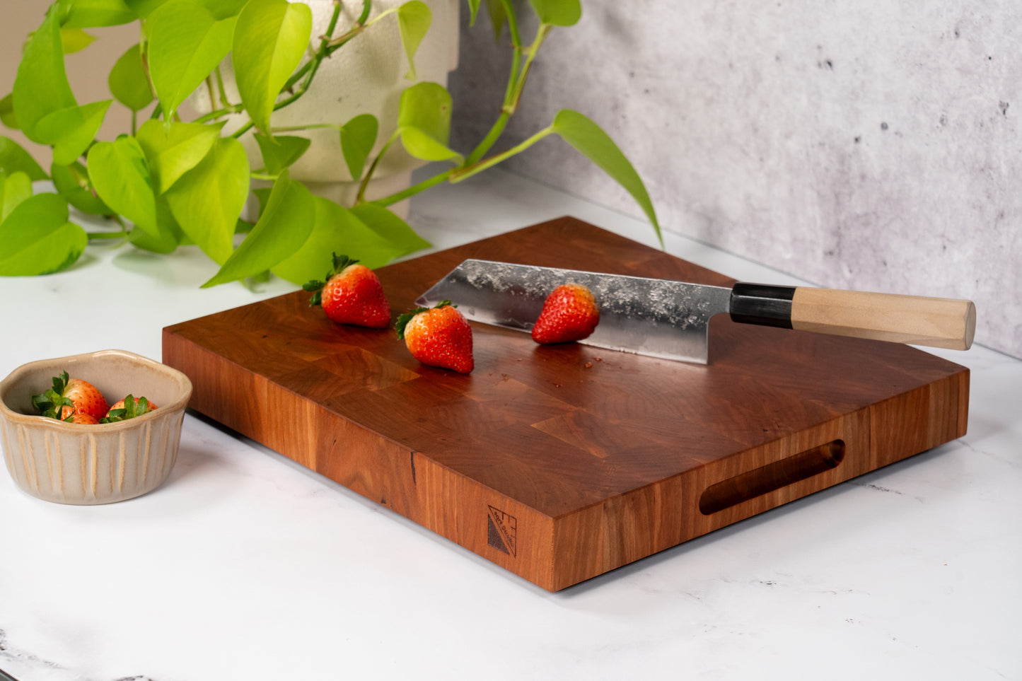 Cherrywood square cutting board on a marble kitchen counter top, bowl of fresh strawberries