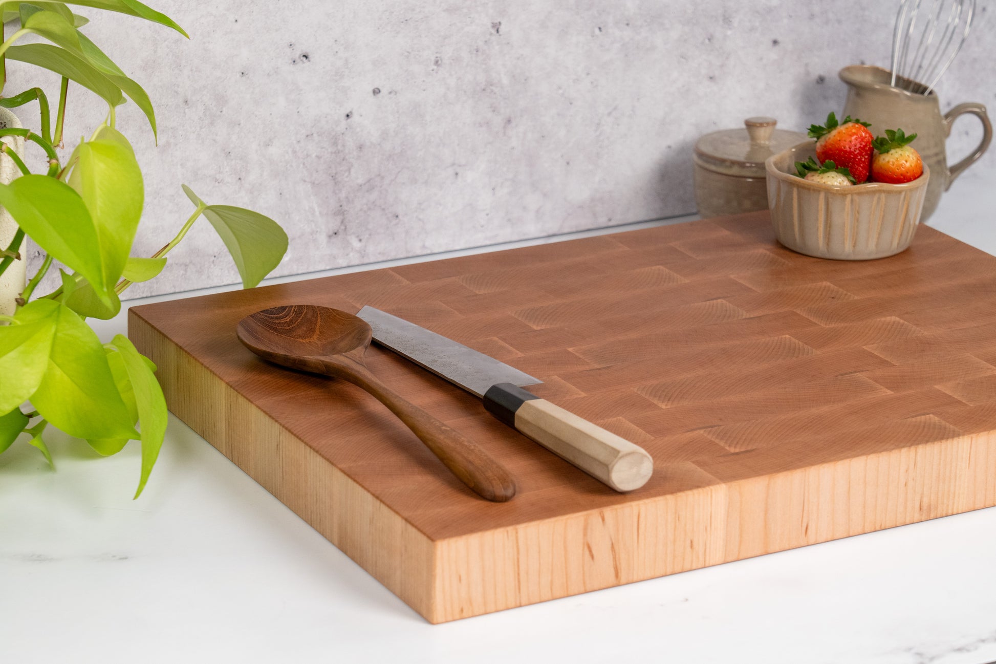 Extra large hard maple butcher block on the kitchen counter, wooden kitchen utensils, fresh strawberries sitting in a bowl on an end-grain cutting board 20x15 made of high-quality hard maple locally sourced in California USA, made in USA Square Root Studio a premium brand making wooden kitchen accessories with great craftsmanship and attention to quality and details