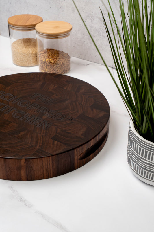 wooden walnut round end grain cutting board on the kitchen counter, butcher block round shape with handles, black american walnut end grain with custom engraving, personalized cutting board ideal as gift for kitchen lovers