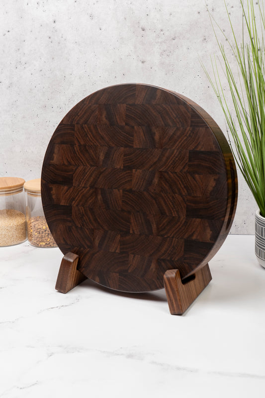 black walnut end grain cutting board placed on a cutting board stand in matching wood pattern, american walnut round butcher block on the kitchen counter, sturdy cutting board stand made out of walnut
