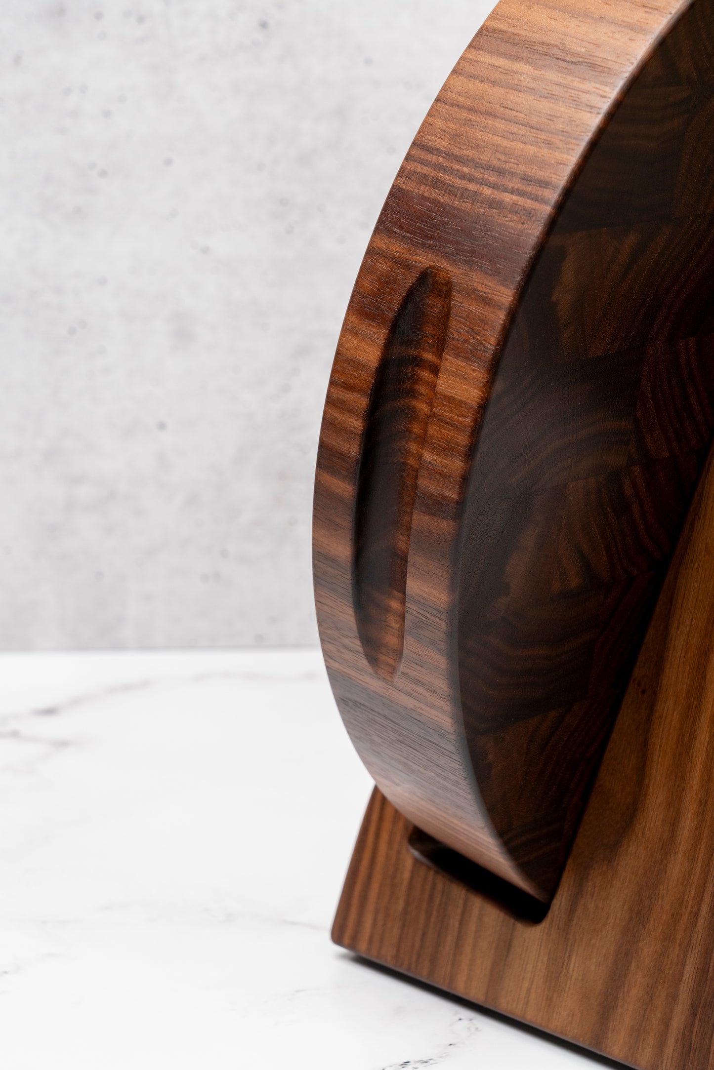 round end grain cutting board with handles for easy lifting and best cooking experience. round cutting board sitting on a walnut cutting board stand