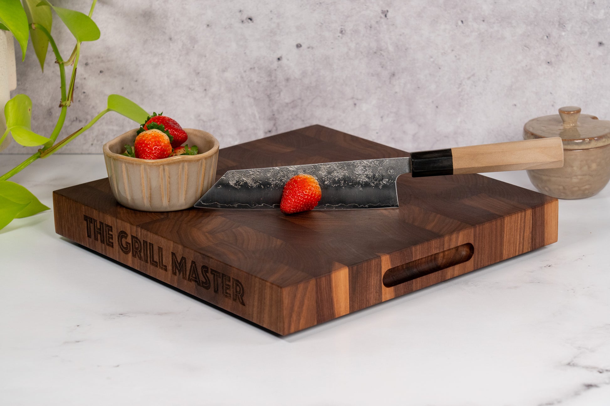 Black American Walnut wood cutting board, end grain pattern, fresh cut strawberries on top, on marble kitchen counter top