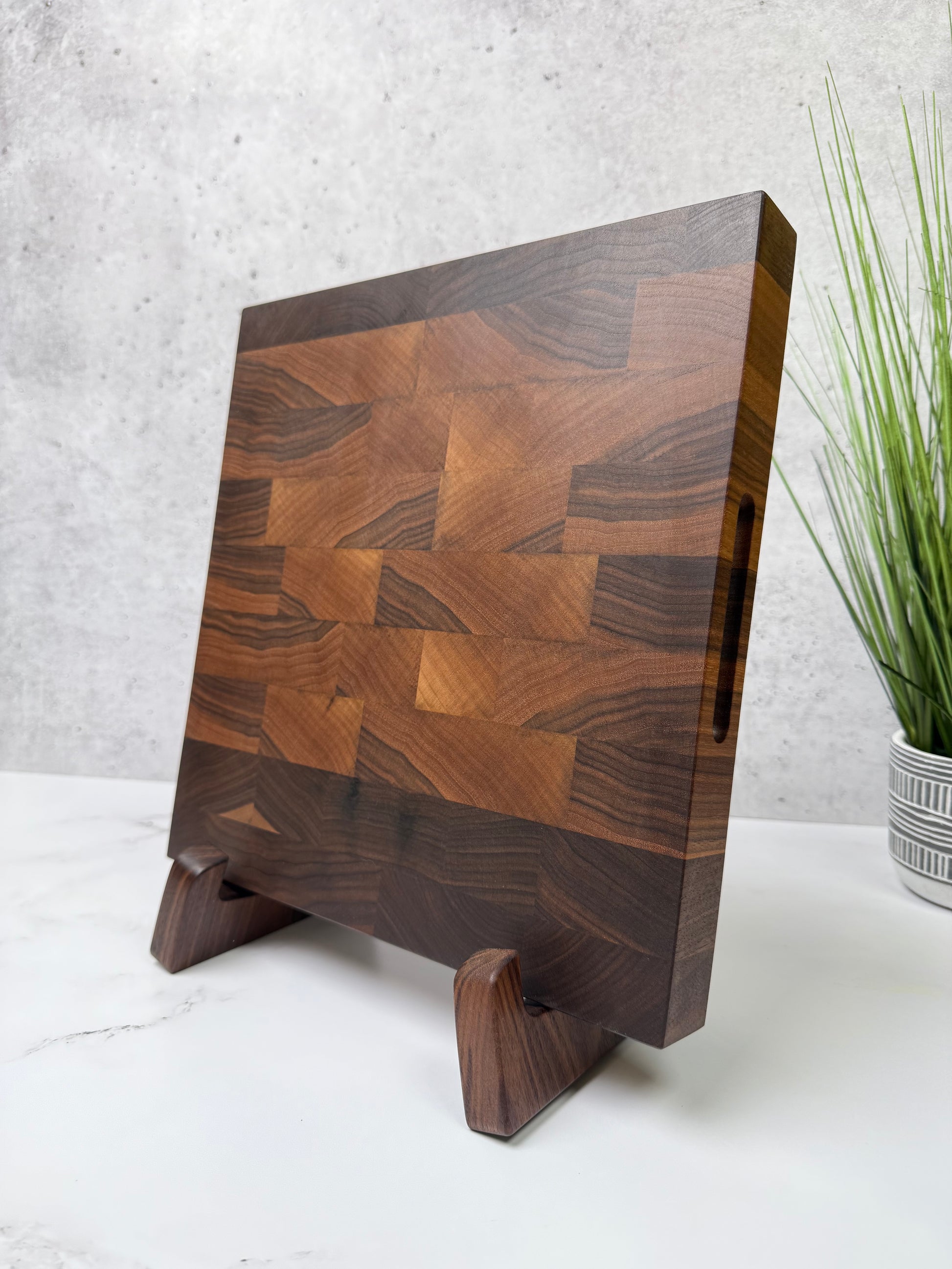Square walnut end grain cutting board sitting on a walnut cutting board stand, the cutting board holder keeps the board at a slight angle and allows for uniform dry and a beautiful display, made in USA by Square Root Studio